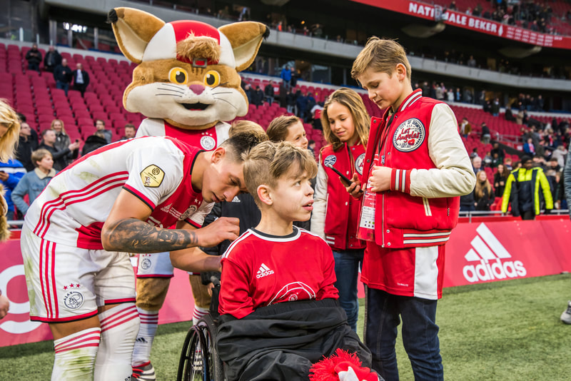 Ajax mascot and supporters pitchside at a home match
